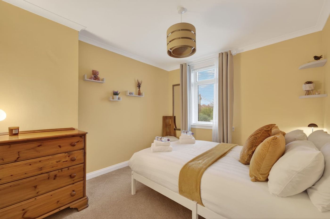 A yellow bedroom with a white wooden bed and towels ready.