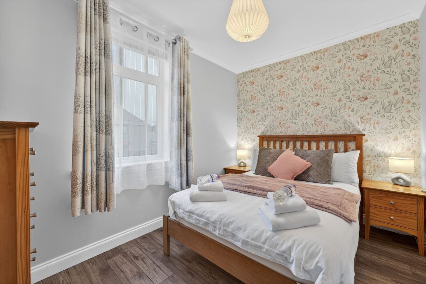 A bedroom with woodland wallpaper, white linen, and bedside lamps.