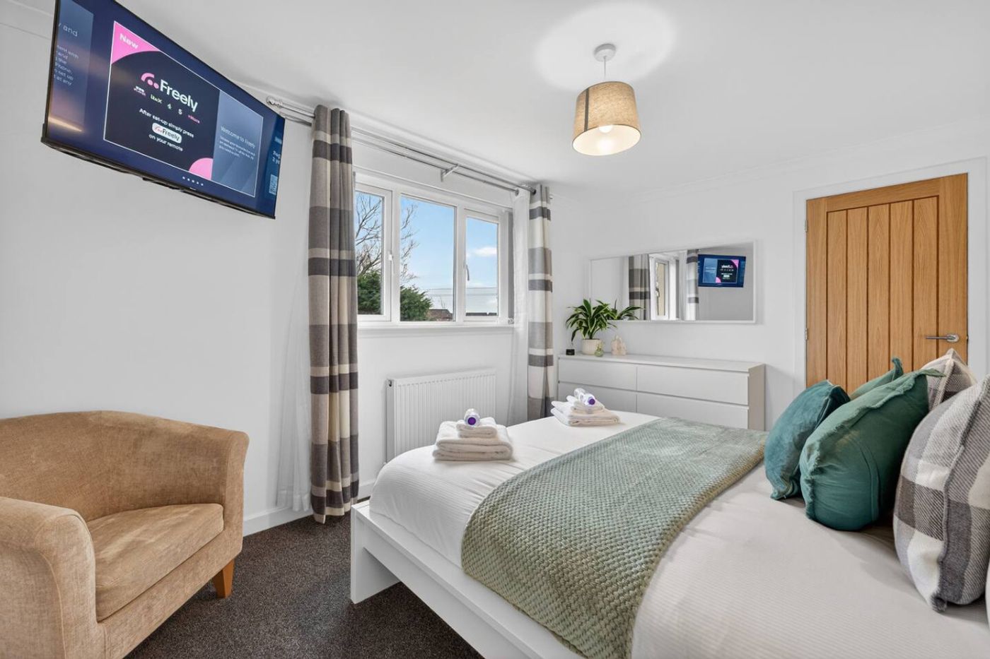 A bedroom with a white bed, armchair, and a television.